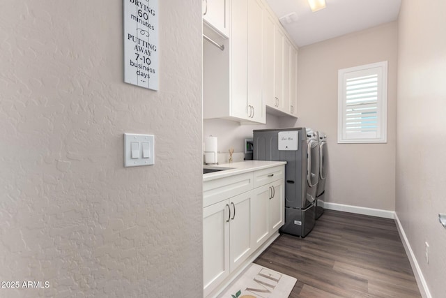 washroom featuring washing machine and dryer, cabinet space, baseboards, and dark wood-style floors