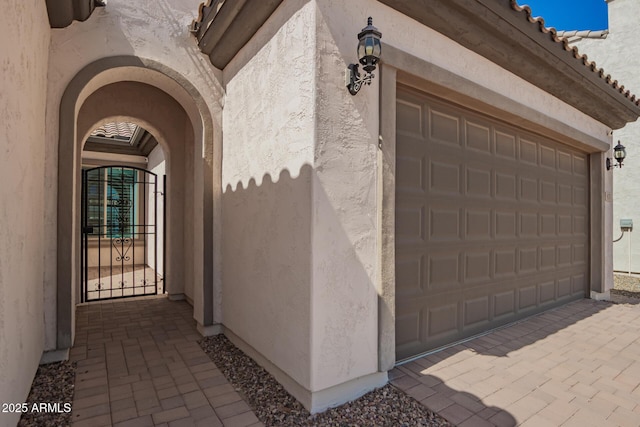 property entrance with stucco siding, a garage, a tile roof, and a gate