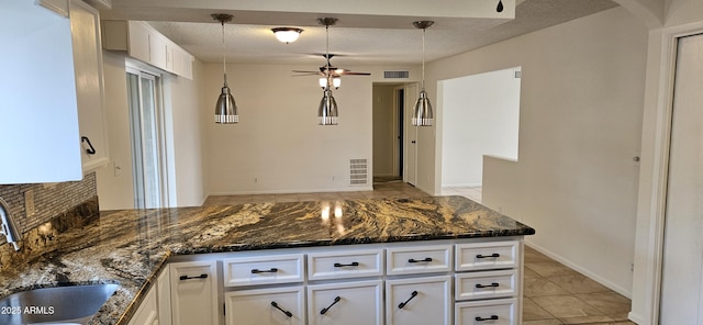 kitchen with white cabinetry, sink, hanging light fixtures, and dark stone countertops