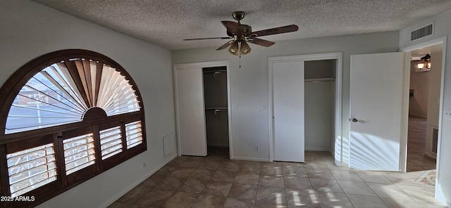 unfurnished bedroom with multiple windows, two closets, tile patterned floors, and ceiling fan