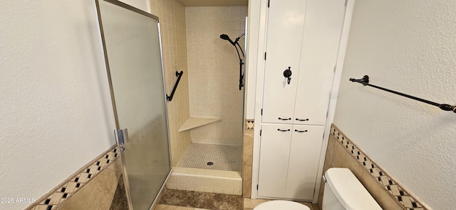 bathroom featuring tiled shower, toilet, and tile walls