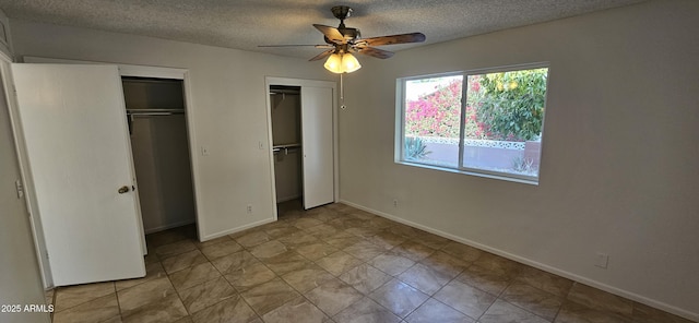 unfurnished bedroom with ceiling fan, a textured ceiling, and two closets