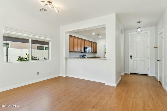 kitchen featuring decorative light fixtures, light hardwood / wood-style flooring, kitchen peninsula, and light stone countertops