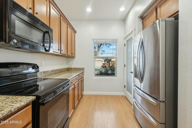 kitchen with black appliances, light stone counters, and light hardwood / wood-style floors