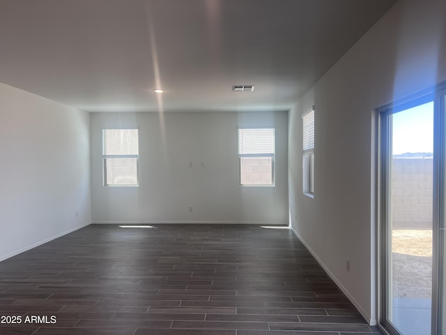 empty room featuring baseboards, dark wood-style floors, and a healthy amount of sunlight