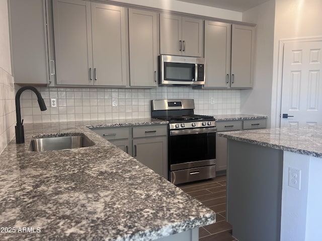 kitchen featuring stainless steel appliances, dark stone countertops, a sink, decorative backsplash, and gray cabinetry