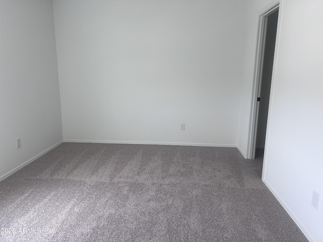 spare room featuring dark carpet and baseboards