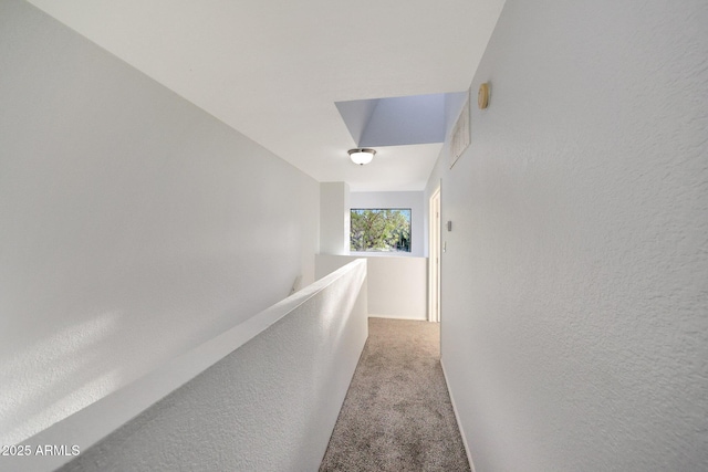 hall with carpet flooring, a textured wall, and an upstairs landing