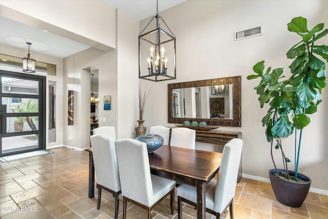 dining area featuring stone tile floors, visible vents, a chandelier, and baseboards