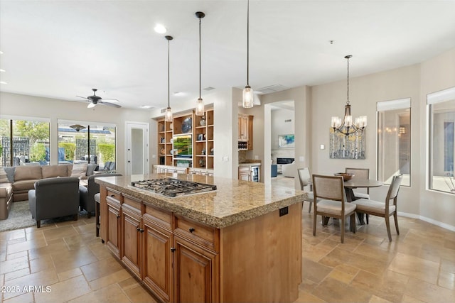 kitchen featuring baseboards, stainless steel gas cooktop, stone tile flooring, open floor plan, and a center island