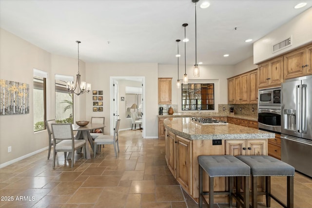 kitchen with a kitchen island, backsplash, stone tile flooring, stainless steel appliances, and baseboards