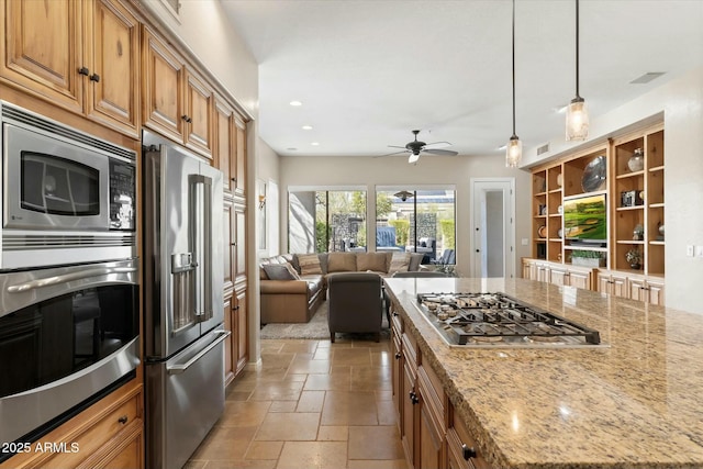 kitchen with open floor plan, stone tile floors, light stone counters, recessed lighting, and appliances with stainless steel finishes