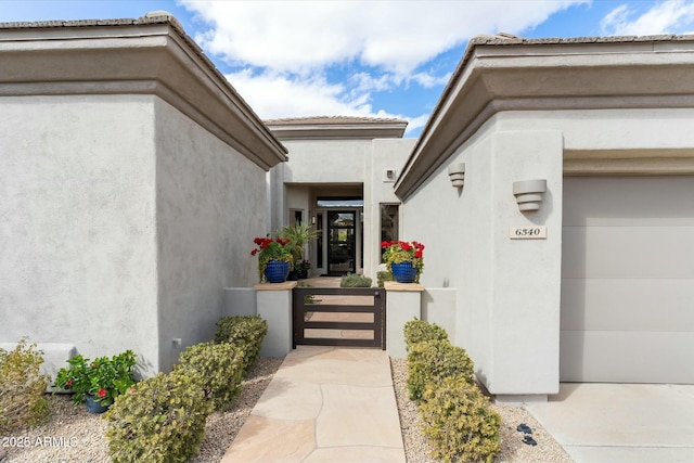 doorway to property featuring stucco siding, a garage, and a gate