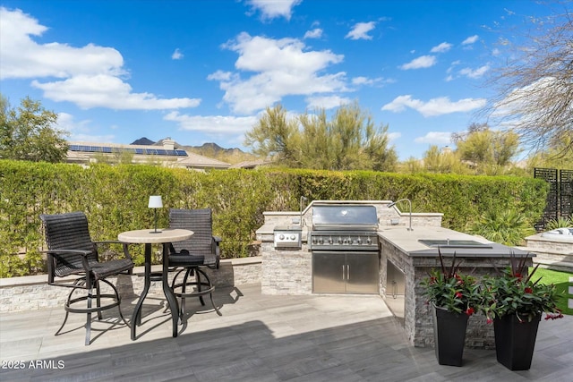 wooden terrace featuring area for grilling, an outdoor kitchen, and a patio