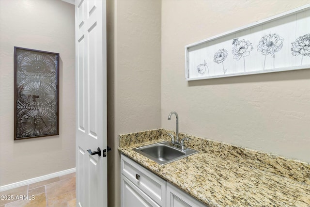 kitchen with a sink, baseboards, light stone counters, and a textured wall