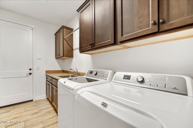 laundry room featuring light wood finished floors, baseboards, washer and clothes dryer, cabinet space, and a sink