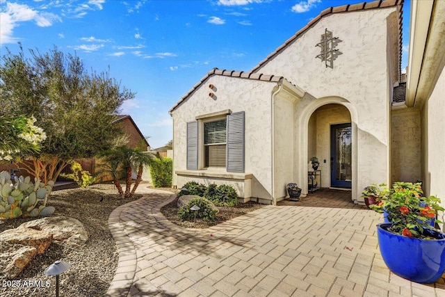 exterior space featuring stucco siding, a tile roof, a patio, and fence