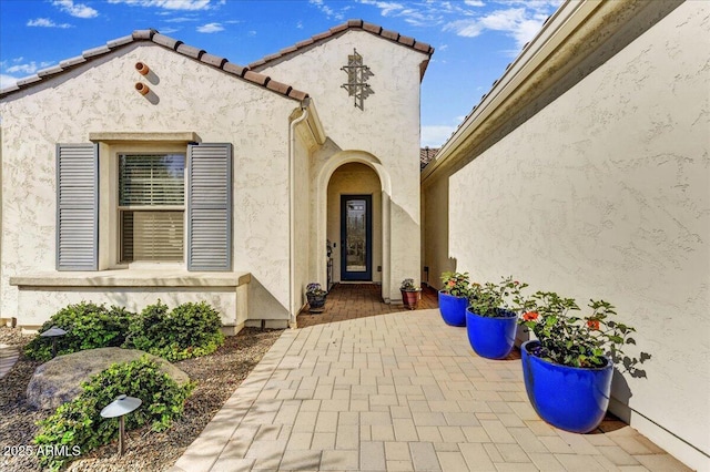 doorway to property with a patio, a tile roof, and stucco siding