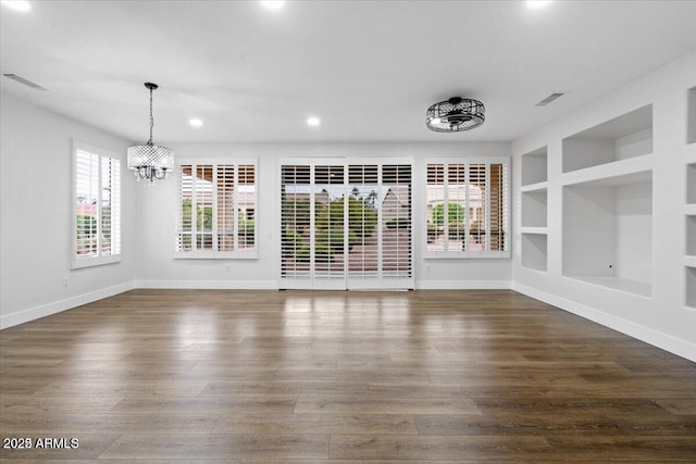 unfurnished dining area with built in features, dark hardwood / wood-style floors, and an inviting chandelier