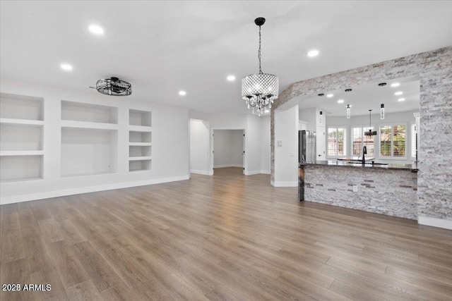 unfurnished living room featuring built in shelves, sink, a chandelier, and light hardwood / wood-style flooring