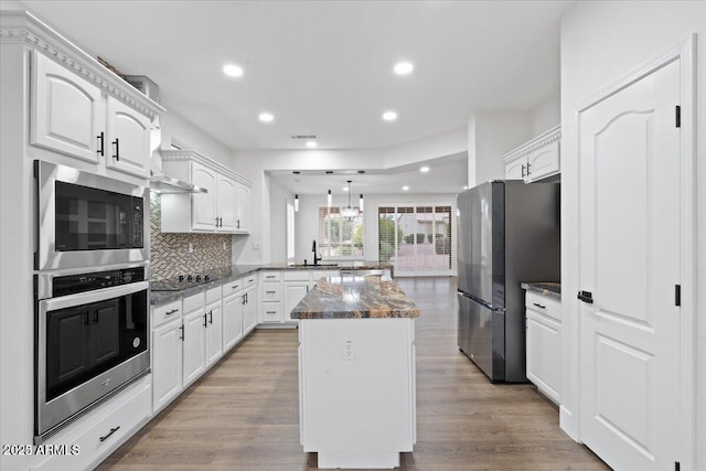 kitchen featuring kitchen peninsula, tasteful backsplash, white cabinets, a center island, and stainless steel refrigerator