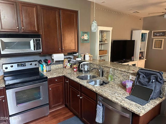 kitchen featuring stainless steel appliances, light stone countertops, sink, dark wood-type flooring, and kitchen peninsula