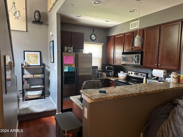 kitchen featuring a breakfast bar, dark hardwood / wood-style flooring, appliances with stainless steel finishes, dark stone countertops, and kitchen peninsula