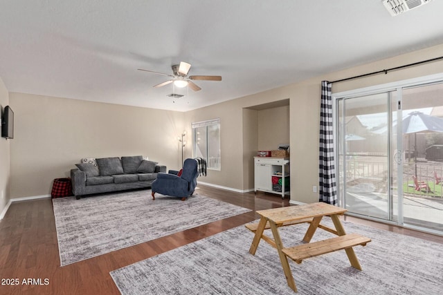 living room with dark wood-type flooring, visible vents, baseboards, and a ceiling fan