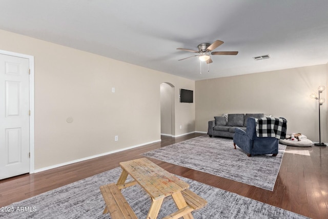 living area featuring arched walkways, wood finished floors, visible vents, baseboards, and a ceiling fan