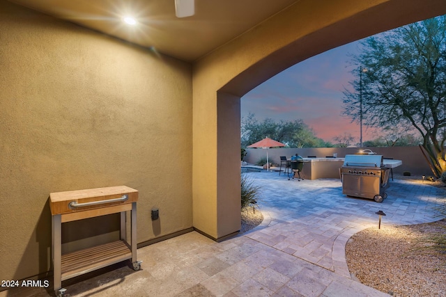 patio terrace at dusk featuring a grill, an outdoor bar, and exterior kitchen