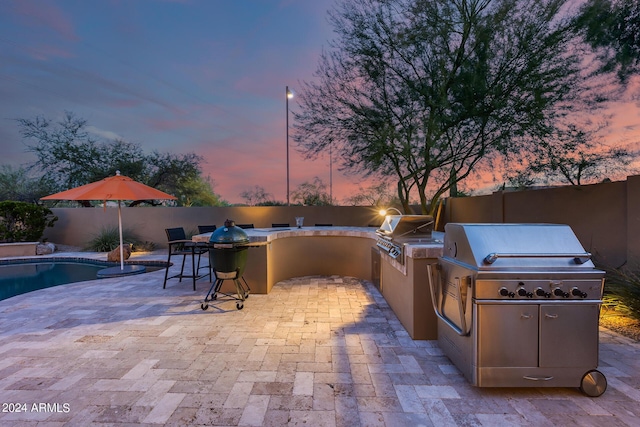 patio terrace at dusk featuring a fenced in pool and area for grilling