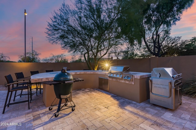 patio terrace at dusk featuring a grill, exterior kitchen, and an outdoor bar