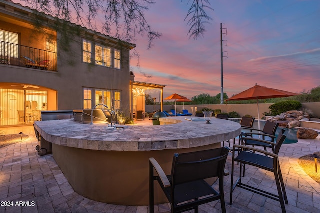 patio terrace at dusk featuring an outdoor bar and exterior kitchen