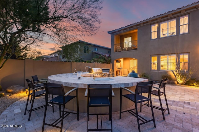 patio terrace at dusk featuring a balcony and an outdoor bar