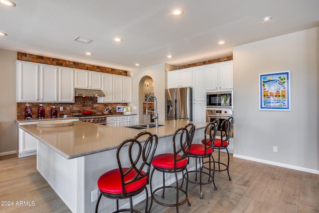 kitchen featuring white cabinets, appliances with stainless steel finishes, a large island with sink, and a breakfast bar area