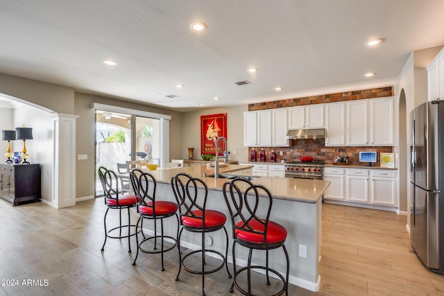 kitchen with appliances with stainless steel finishes, backsplash, a kitchen breakfast bar, white cabinets, and an island with sink