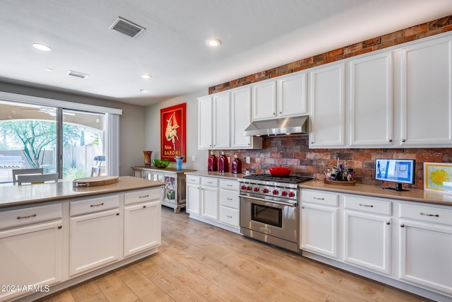 kitchen with tasteful backsplash, white cabinetry, luxury stove, and light hardwood / wood-style floors