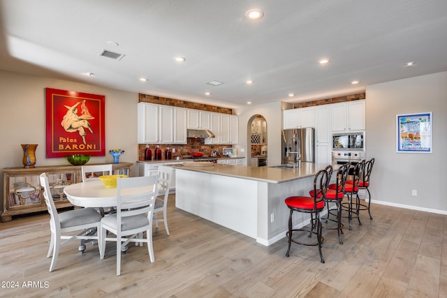 kitchen with white cabinets, a large island, light wood-type flooring, and stainless steel appliances