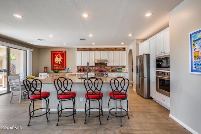 kitchen with a kitchen island with sink, white cabinets, tasteful backsplash, a breakfast bar area, and stainless steel appliances