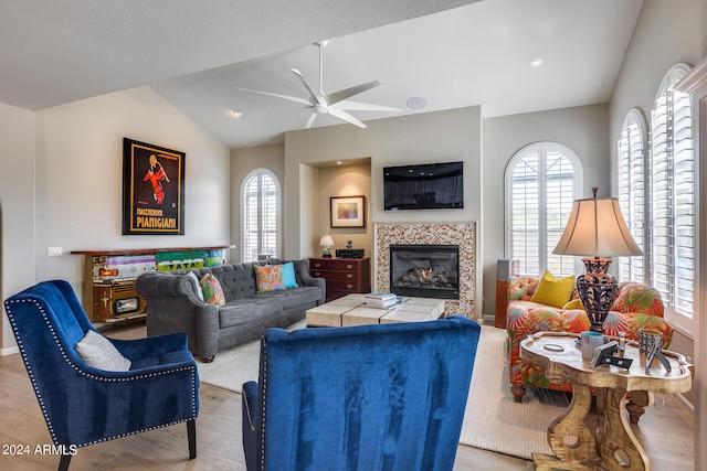 living room featuring vaulted ceiling, light hardwood / wood-style flooring, ceiling fan, and a tiled fireplace