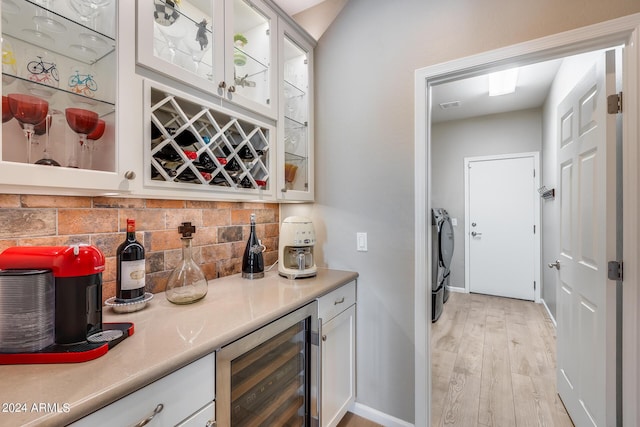 bar with tasteful backsplash, wine cooler, washing machine and clothes dryer, and white cabinets