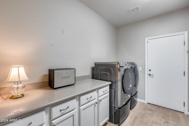 clothes washing area with washer and clothes dryer, cabinets, and light hardwood / wood-style flooring