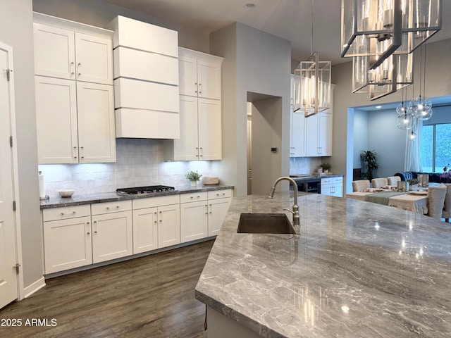 kitchen featuring dark wood-style flooring, stainless steel gas cooktop, tasteful backsplash, white cabinetry, and a sink