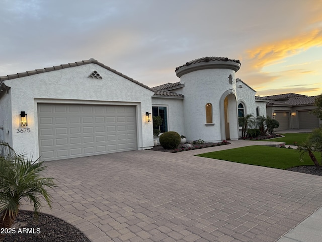 mediterranean / spanish-style house featuring an attached garage, a tile roof, decorative driveway, and stucco siding