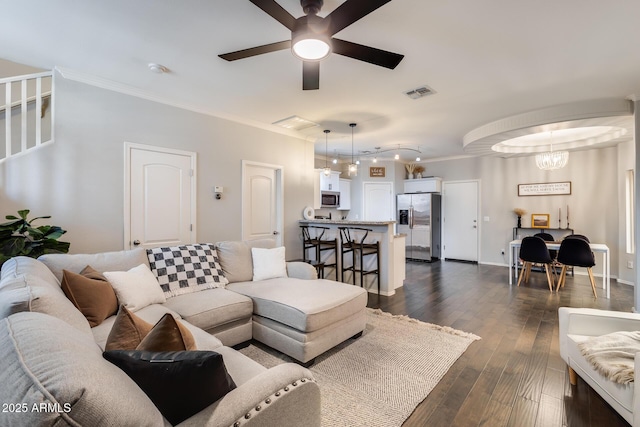 living room featuring crown molding, dark wood-type flooring, and ceiling fan with notable chandelier