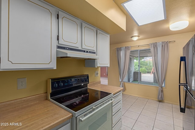 kitchen featuring under cabinet range hood, range with electric stovetop, freestanding refrigerator, light tile patterned flooring, and light countertops