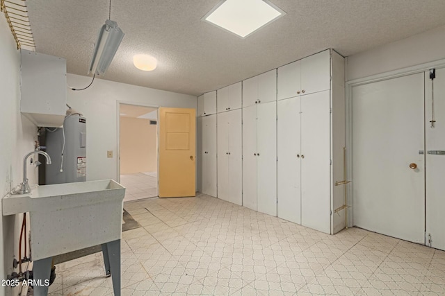 kitchen with a sink, a textured ceiling, water heater, white cabinetry, and light floors