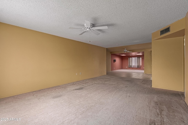 carpeted spare room featuring a textured ceiling, visible vents, and ceiling fan