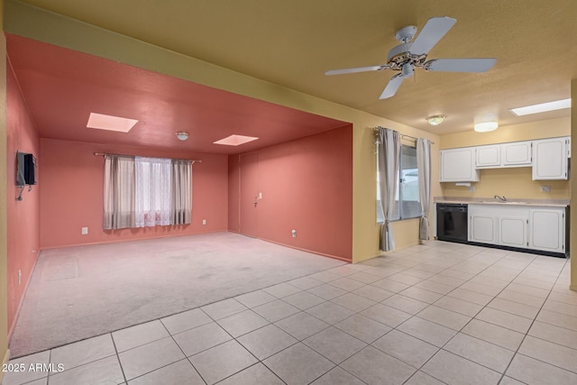 unfurnished living room featuring light carpet, a ceiling fan, a sink, a skylight, and light tile patterned floors