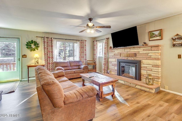 living area featuring a stone fireplace, wood finished floors, a ceiling fan, and baseboards